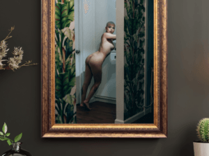 Fine art nude of Madam Sophie in LA, leaning elegantly in a hallway framed by vibrant tropical wallpaper, exuding strength and sophistication